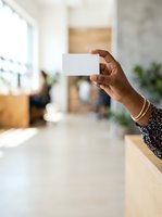 Woman with dark skin tone holding blank white business card in modern office interior with natural light, suitable for corporate branding and professional marketing materials.