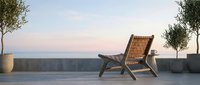 Wooden lounge chair on modern rooftop terrace at sunset with potted trees and concrete wall, ideal for hospitality and lifestyle design projects.