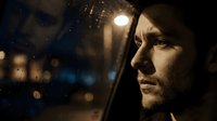 Contemplative man gazing through rain-covered window at night with city lights creating atmospheric bokeh background for emotional storytelling concepts.