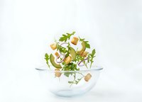 Fresh arugula salad with croutons in glass bowl isolated on white background for healthy eating and culinary design projects.