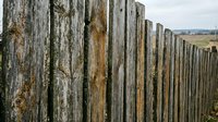 Weathered wooden fence posts create rustic boundary in rural countryside landscape with rolling hills and farmland stretching into distance under cloudy sky.