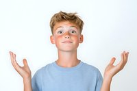 Young boy in light blue t-shirt expressing surprise and wonder with raised hands and upward glance against white background, showing genuine emotion and curiosity.