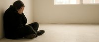 Young woman sitting alone on floor in empty room experiencing depression, sadness and mental health struggles in minimalist indoor space.