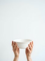 Hands holding empty white ceramic bowl against neutral background, studio shot for product presentation and kitchenware concepts.