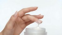 Caucasian woman's hand applying moisturizing cream or skincare product from jar, isolated on white background for cosmetics and beauty design use.
