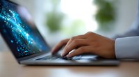 Professional hands typing on laptop keyboard with glowing blue digital particles effect, modern workplace setting with soft background blur.