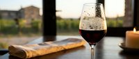 Glass of red wine on wooden table with candle creating warm ambiance for romantic dinner or evening relaxation at home during golden hour sunset.