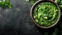 Fresh homemade chimichurri sauce with parsley, garlic and olive oil in rustic ceramic bowl on dark stone background with copy space for menu design.