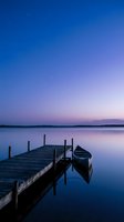 Wooden dock with moored boats on calm lake at twilight, stars visible in deep blue sky transitioning to purple horizon, serene water reflection, ideal for travel and nature backgrounds.