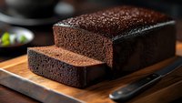 Fresh baked dark chocolate bread loaf sliced on wooden cutting board with knife, homemade dessert bakery product for breakfast or snack time.