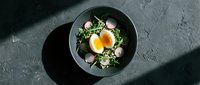 Overhead view of a gourmet salad bowl with fresh greens, microgreens, and two sunny-side-up eggs on dark plate. Perfect for food blogs, restaurant menus, and culinary content.