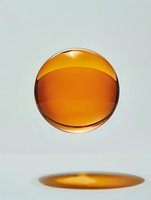 Amber liquid sphere floating with shadow reflection on light background, showcasing transparency and gravitational suspension in minimalist setting.