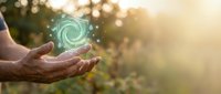 Hand holding glowing spiral energy symbol with particles against blurred nature background, representing renewable power, sustainability, and eco-friendly technology concepts.