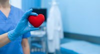 Healthcare professional in blue scrubs holding red heart symbol representing cardiology care and medical compassion in clinical setting.
