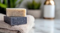 Natural handmade soap bars with herbs and charcoal on beige cotton towel against blurred bathroom setting, spa and wellness concept for skincare.