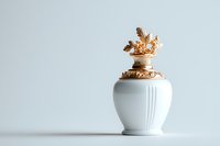 Elegant white ceramic urn with ornate gold decorative lid featuring leaf motifs, photographed against light background. Suitable for memorial and decorative concepts.