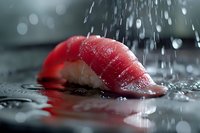Fresh tuna sashimi slice with water droplets splashing in dramatic lighting, raw fish on dark reflective surface creates luxurious culinary atmosphere.