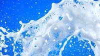 White foam bubbles splashing against vibrant blue water background creating dynamic liquid motion for cleaning and freshness concepts.