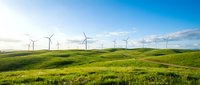 Wind turbines generating clean renewable energy across vast green rolling hills under bright blue sky.