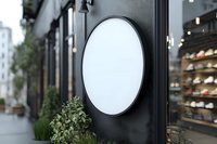 Blank oval signage on black storefront facade with green plants and urban street view, suitable for restaurant, retail, or cafe branding mockups.