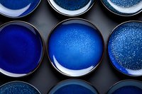 Handcrafted ceramic plates with deep blue glazed surface showing various textural patterns and speckled effects on dark background, arranged in rows.