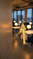 Hand holding glowing golden arrow pointing upward with sparkling particles in modern office space with city skyline view and warm ambient lighting for business growth concepts.