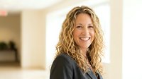 Professional blonde businesswoman with curly hair smiling confidently in modern office environment. Corporate executive portrait for business presentations.