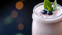 Creamy protein smoothie with fresh blueberries, mint leaves and chocolate sprinkles in glass jar on dark background with bokeh lights. Healthy breakfast concept.