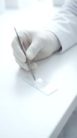 Gloved hand holding tweezers places a sample on a glass microscope slide in a clean laboratory setting for medical research.