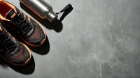 Pair of athletic sneakers with orange and black mesh design next to water bottle on gray concrete surface for fitness and sports marketing.