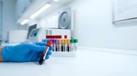 Medical laboratory technician hand in blue glove holding blood sample tube with colorful test tubes rack in sterile clinical environment for analysis.