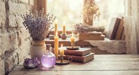 Cozy rustic still life with lavender bouquet, burning candles, vintage books and amethyst crystals on wooden table creating warm atmospheric home decor scene.