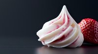 Swirled white meringue with pink streaks and fresh strawberry on dark background, soft focus food photography highlighting dessert texture and detail.