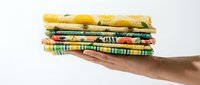 Stack of colorful folded fabric pieces with floral and citrus prints held in hand, perfect for sewing, quilting, and textile craft projects.