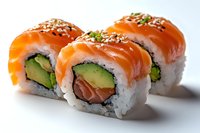 Fresh salmon and avocado sushi rolls topped with raw fish, sesame seeds and green onion on white background, close up view of Japanese cuisine.