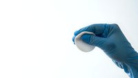 Medical professional in blue latex gloves holding breast implant for cosmetic surgery consultation and patient education on white background.