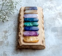 Colorful healing crystals arranged in chakra order on rustic wooden block with baby's breath flowers, spiritual wellness concept for meditation and energy healing.