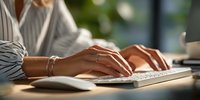 Professional woman typing on white keyboard at modern office desk with natural lighting for business and productivity content.