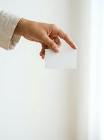 Adult hand with medium skin tone holding blank white card against neutral background for branding, business card mockup, or corporate identity presentation.