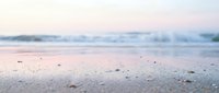 Serene sandy beach at dawn with soft waves and misty horizon, peaceful coastal landscape for relaxation and travel themes.