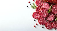 Sliced salami with rosemary sprigs and peppercorns on white background. Traditional cured meat arrangement for appetizer or charcuterie board styling.