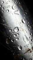Water droplets on brushed metal surface with scratches and weathered texture creating industrial background for manufacturing and engineering projects.