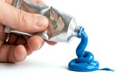 Hand squeezing blue acrylic paint from metal tube onto white surface for artistic projects and creative work.