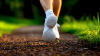 Close-up view of white running shoe on dirt trail during morning jog, with blurred green nature background and sunlight creating warm atmosphere.