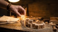 Hand placing wooden cube with lightbulb icon among business symbol blocks on craftsman workbench in warm workshop lighting for creative solutions.