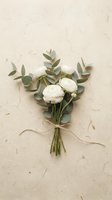 White ranunculus flowers and eucalyptus leaves arranged in elegant bouquet tied with ribbon on textured paper background for wedding and romantic occasions.