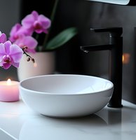 Modern bathroom interior with white vessel sink, black faucet, pink orchid and burning candle creating relaxing spa atmosphere on marble countertop.