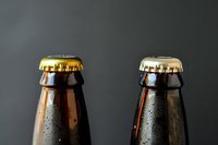 Close-up of two dark glass bottles with metal caps showing condensation droplets against dark background, minimalist composition for beverage advertising.