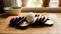 Fresh sliced eggplant with whole egg on wooden cutting board in bright kitchen setting for healthy cooking and meal preparation recipes.
