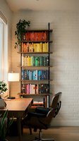Modern home office with colorful rainbow bookshelf organization system against white brick wall featuring wooden desk and leather chair for productivity.